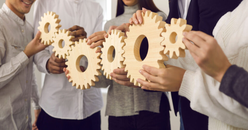 A team of young people making a gear chain as a metaphor for collaboration, coordinated group work, teamwork, professional interaction, building a solid company, and a practical, well-functioning business system using Dynamics 365 Business Central Wave 2