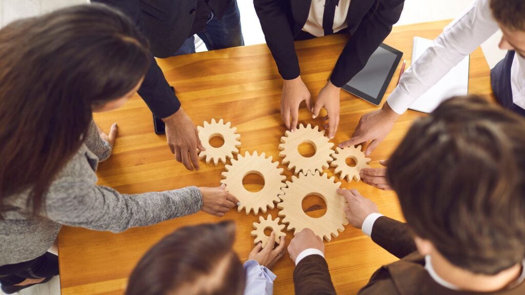 Team collaborating with interlocking gears on a table, symbolizing improved system integration and operational efficiency with Business Central 2025 Release Wave 1.