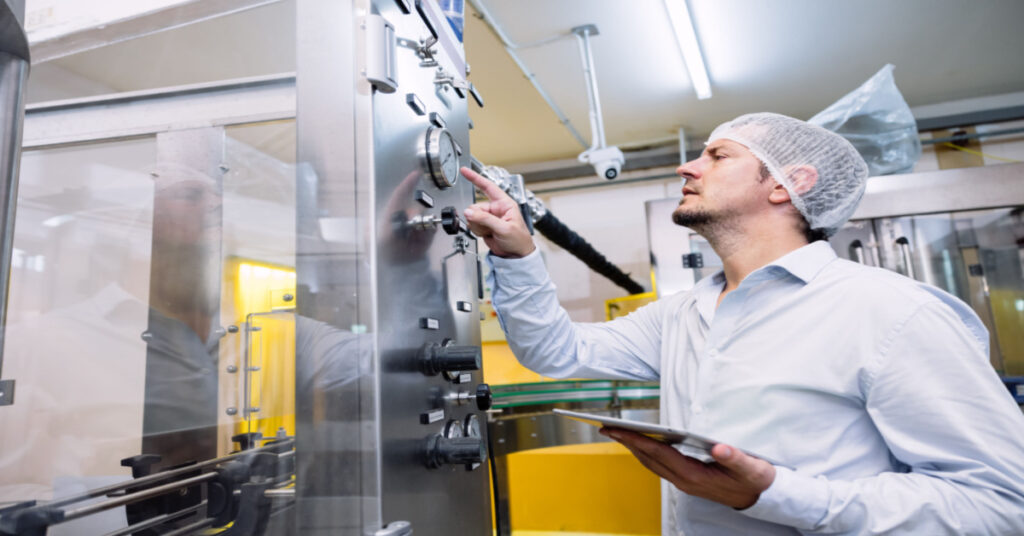A male engineer is working on setting up an automatic machine in a food and beverage industry production facility | Shop Floor Productivity